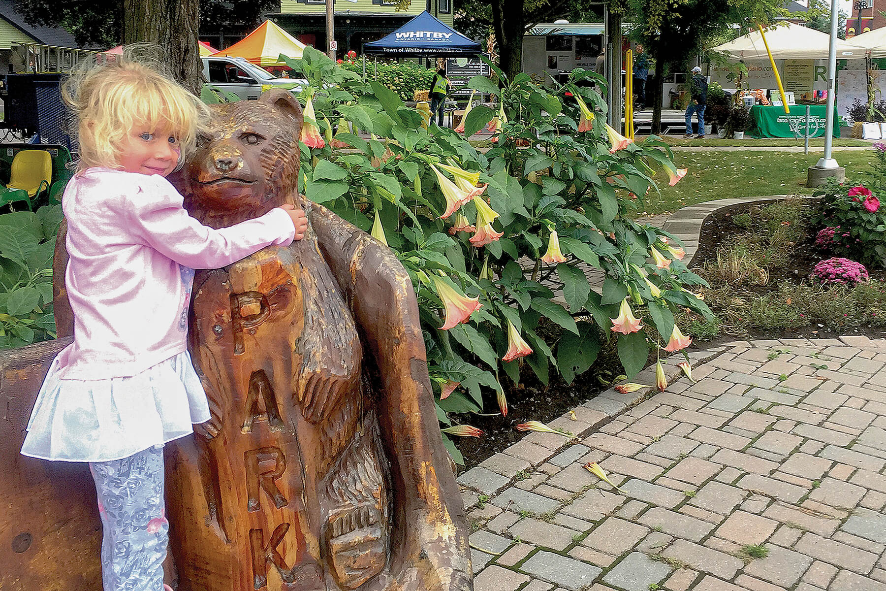 young child hugging a carved wooden bear statue in a garden