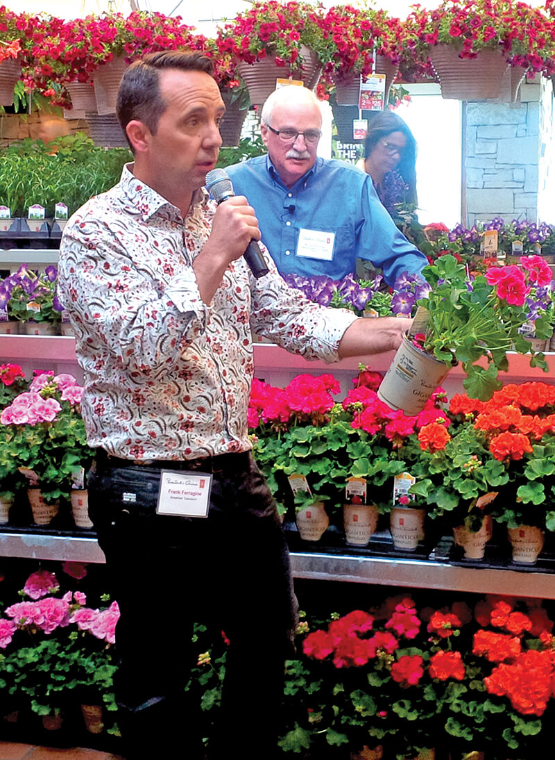 man with microphone speaking in a greenhouse full of plants
