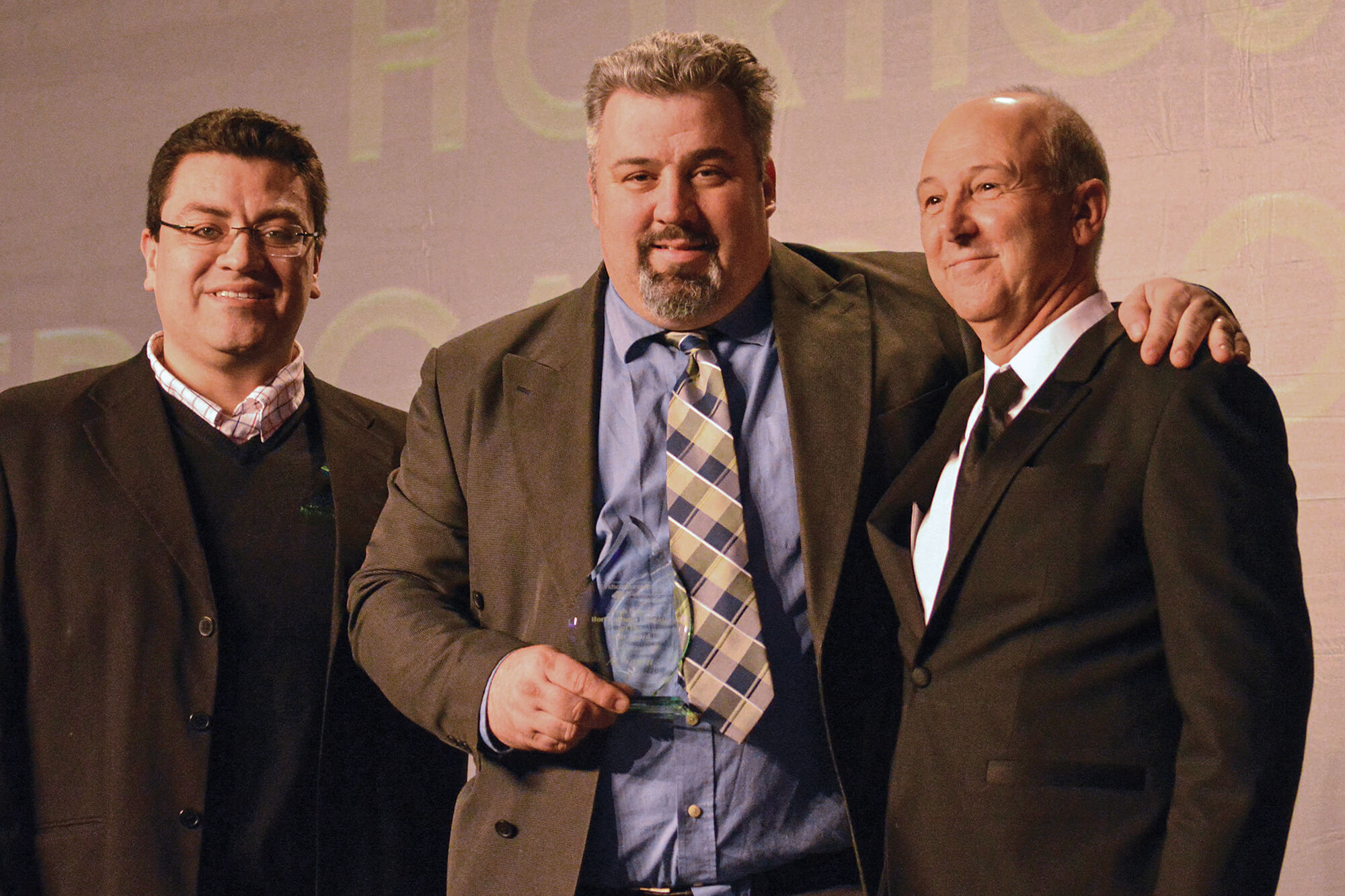 three men on stage, one holding and award