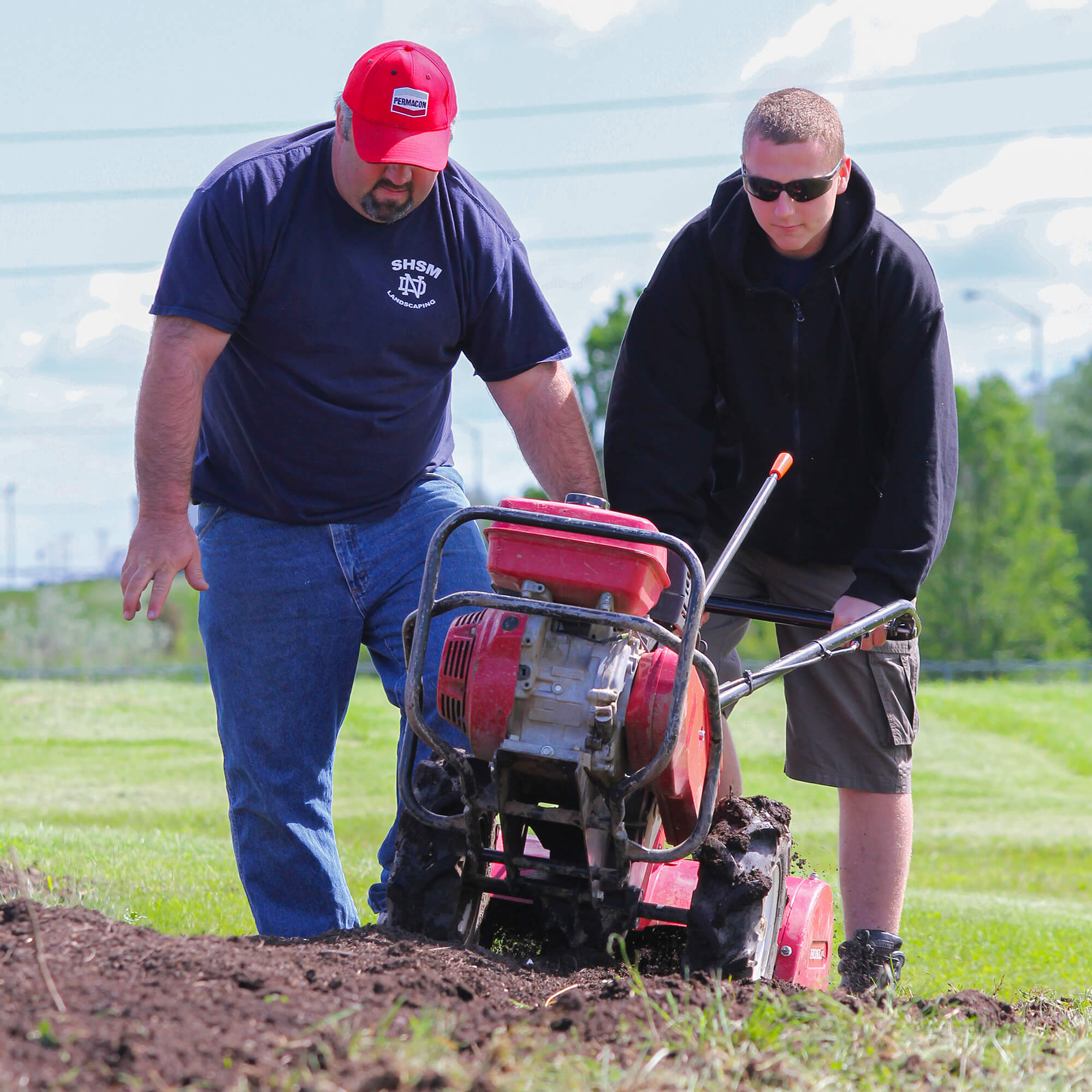 man helping a student use a large rototiller