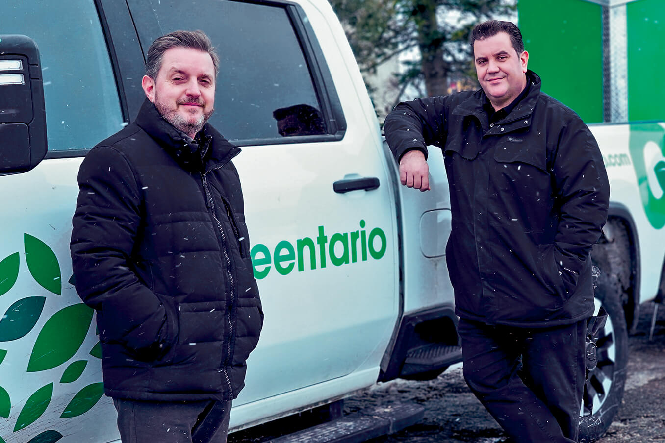 two men standing in front of a company pick up truck